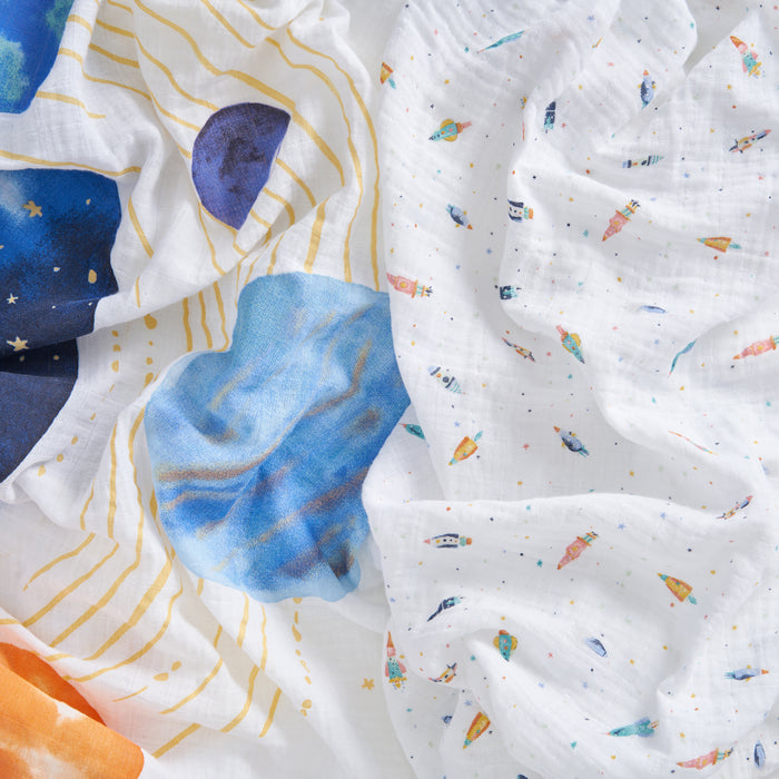 Aden + anais organic cotton muslin swaddle blanket 2 pack features soft, white swaddles with playful, colorful space-themed prints—planets, rockets, stars, and galaxies—in a whimsical pattern. The blankets are gentle and slightly textured.