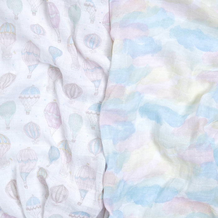 Two pieces of aden + anais fabric: the left with pastel hot air balloons, the right with watercolor clouds in soft blue, pink, and yellow. Both have an airy texture, ideal for crafting sustainable swaddles from organic cotton muslin swaddle blanket 2 packs.