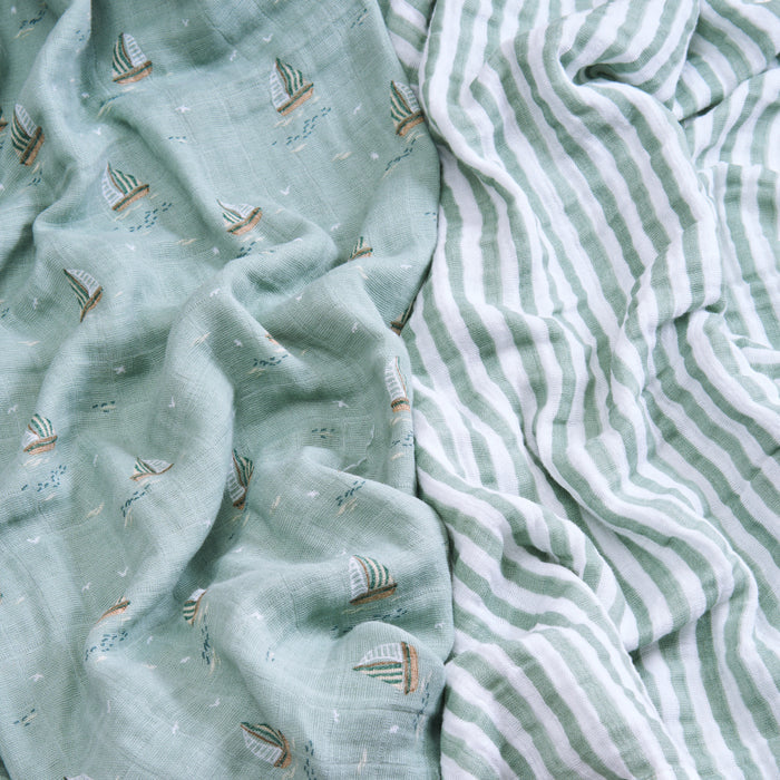 Two soft fabrics are displayed: a pale green with small sailboats and another with white and pale green stripes. Both have a crinkled texture, GOTS certified, ideal for crafting aden + anais organic cotton muslin swaddle blankets.