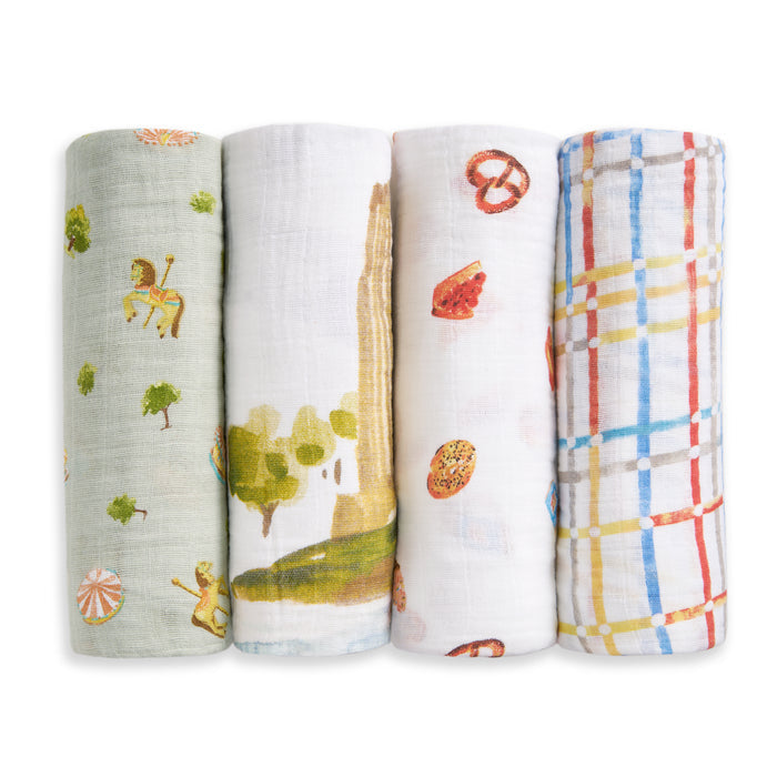The aden + anais organic cotton muslin swaddle blanket 4 pack includes playful designs: green with circus animals, white with a park scene, white with assorted snacks, and white with a colorful plaid pattern.