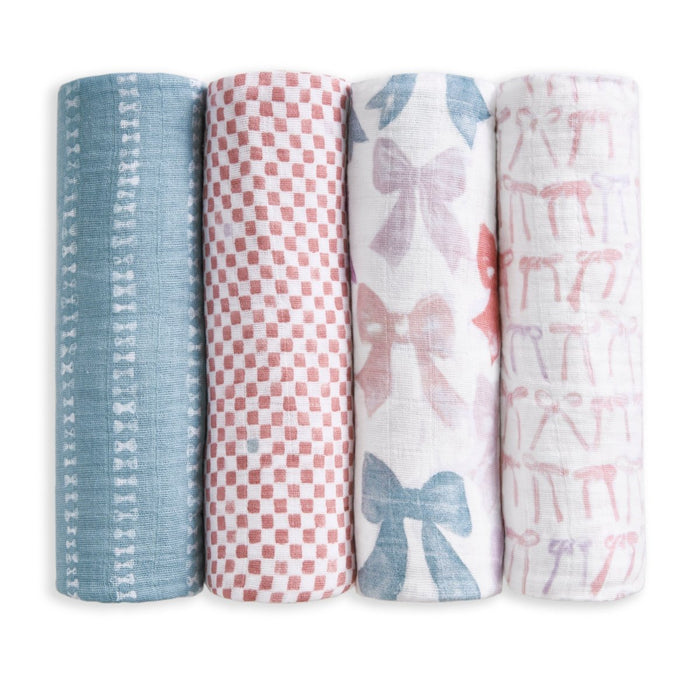 The aden + anais organic cotton muslin swaddle blanket 4 pack features four rolled blankets, each with unique patterns: blue with white bows, red and white checks, large blue and pink bows, and pink bows on white.