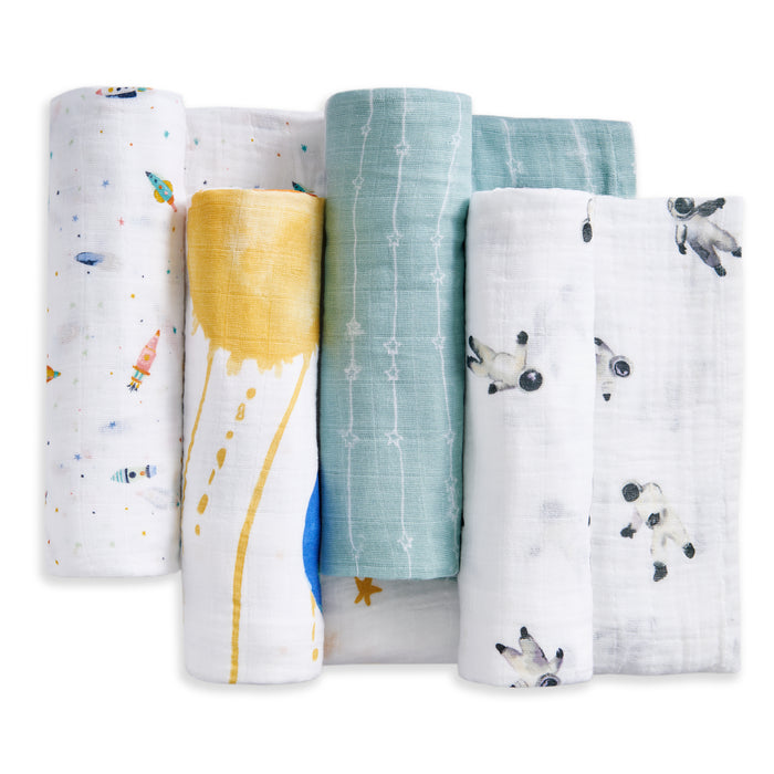 Four organic cotton muslin swaddle blankets by aden + anais are rolled side by side, each featuring a unique design: rockets, yellow suns, blue stripes, and star constellations.
