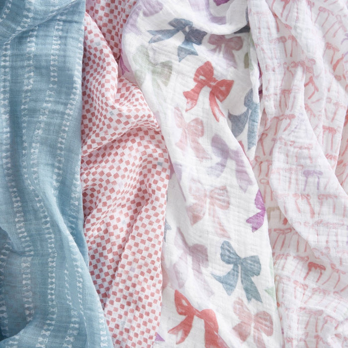The aden + anais organic cotton muslin swaddle blanket 4 pack includes blue with white stripes, pink with red dots, white with multicolored bows, and white with pink bows—soft and perfect for baby's comfort.