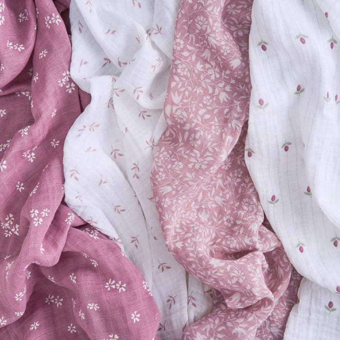 Aden + Anais presents an eco-friendly arrangement of soft, GOTS-certified organic cotton muslin swaddle blankets in shades of white and dusty pink with delicate floral patterns, enhancing style and conscience.