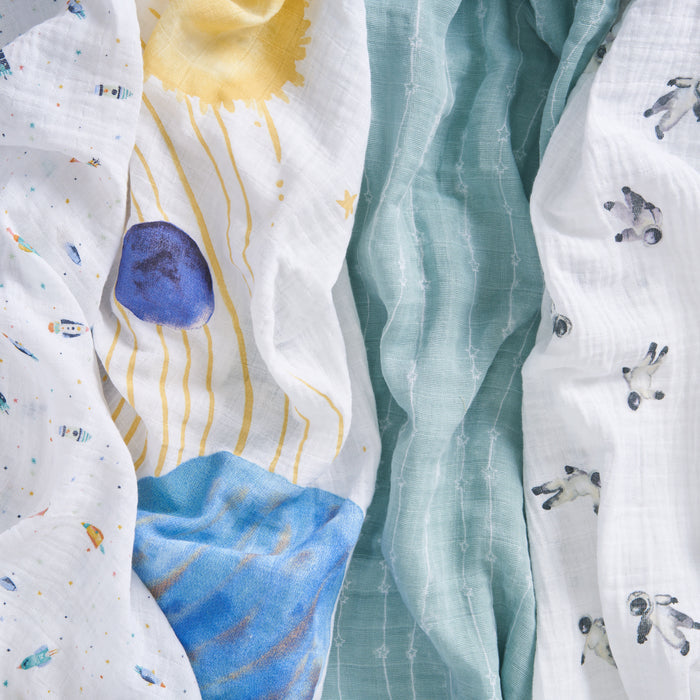 The aden + anais organic cotton muslin swaddle blanket 4 pack is shown: one with space designs, one with a sun and blue planet, one solid teal with a white grid, and one featuring small astronaut illustrations.