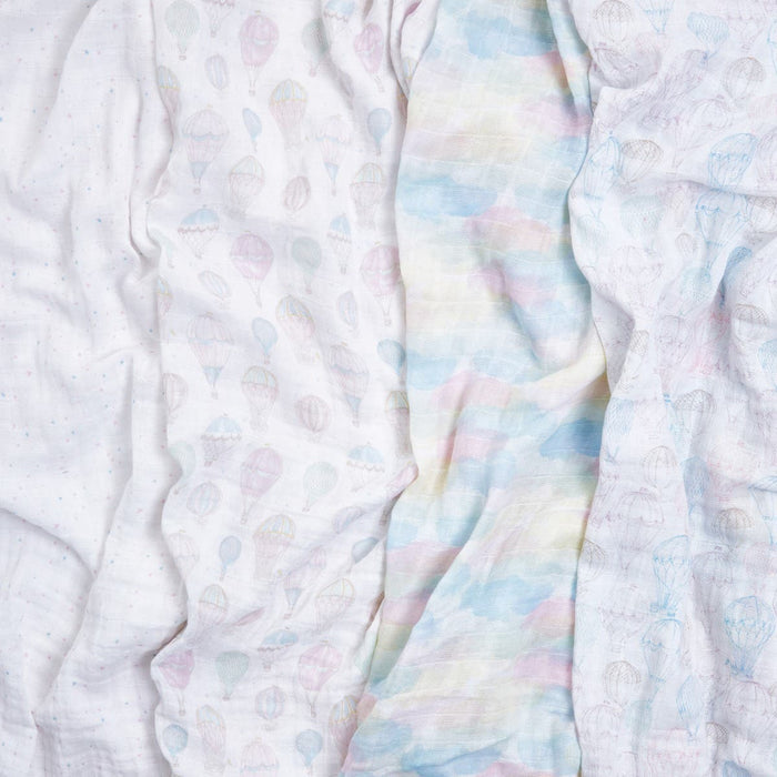 Three organic muslin swaddle blankets from aden + anais, known for their sustainable and GOTS certified design, are displayed: the left one is white with small dots, the middle features pastel clouds, and the right has a hot air balloon pattern.