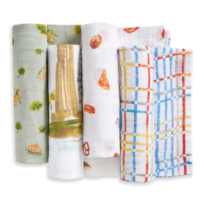 The aden + anais organic cotton muslin swaddle blanket 4 pack features four swaddles with unique prints: green with trees and rides, cityscape with fountain, white with pizza and snacks, and plaid in red, blue, and yellow.