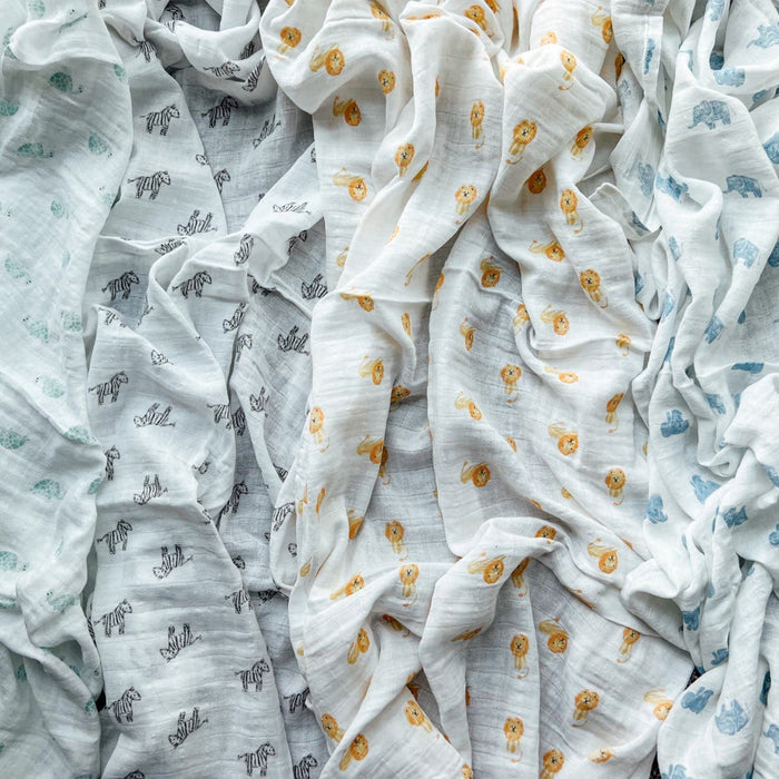 The aden + anais organic cotton muslin swaddle blanket 4 pack features crinkled fabric with diverse patterns: black cursive hello, cheerful yellow lion faces, and playful blue elephants on white and light grayish-blue hues, all GOTS certified for peace of mind.