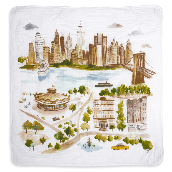 The aden + anais organic cotton muslin dream blanket showcases a watercolor-style city skyline with a river, bridge, carousel, park, fountain, buildings, trees, a boat, and yellow taxi.