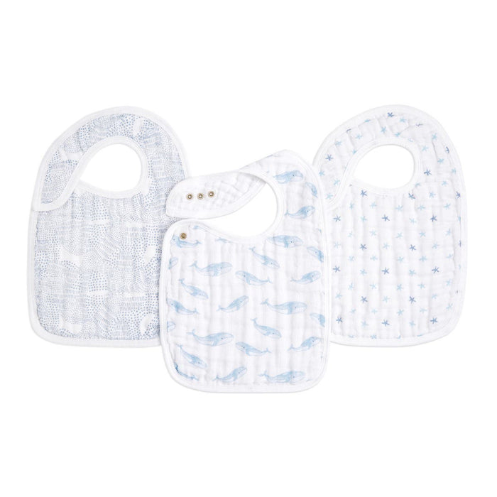 The aden + anais organic cotton snap bibs 3 pack features charming designs—dots, blue whales, and tiny stars. Made from absorbent muslin and GOTS certified, each bib has a convenient top snap closure and is displayed on a white background.