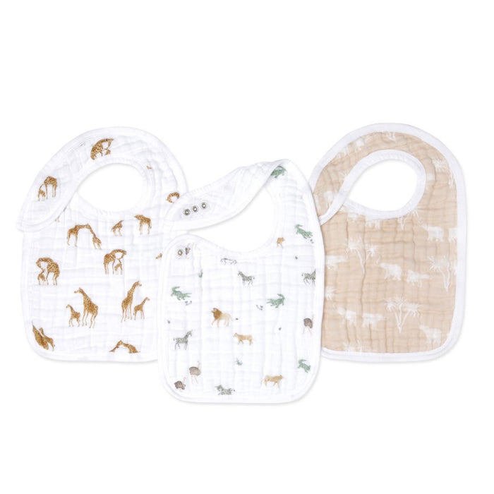 The aden + anais organic cotton snap bibs 3 pack features quilted textures, adjustable fit, and rounded edges. The set includes three bibs: one with giraffes, another with zoo animals, and the third beige with white palm tree patterns.