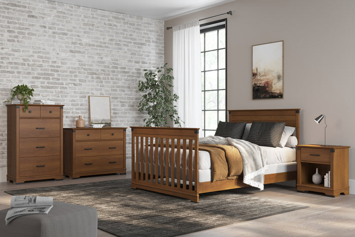 A modern bedroom features wooden furniture—a bed, dresser, chest, and the Child Craft Redmond Nightstand in Coach Cherry—on a dark rug. A large window, potted plant, brick accent wall, and framed art create a cozy, neutral setting.