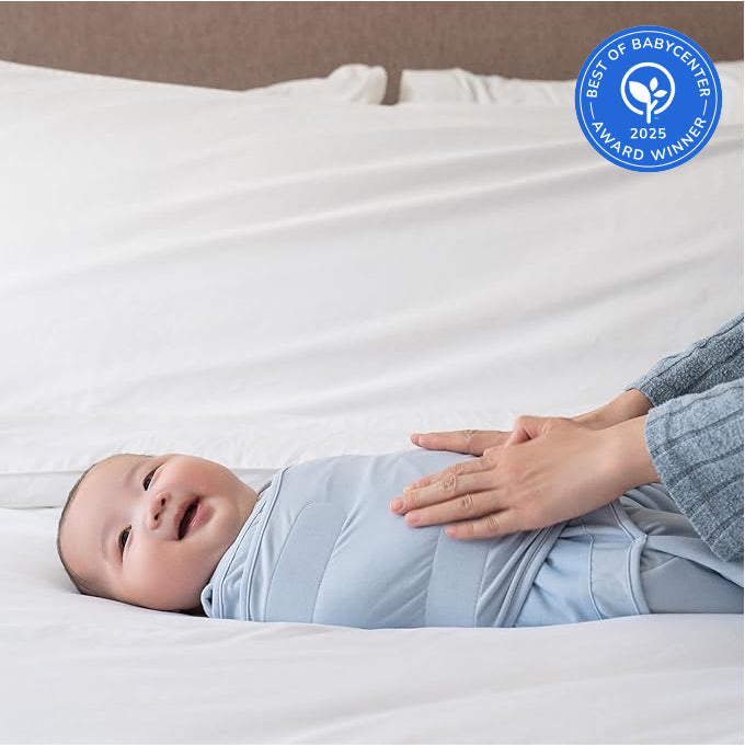 A smiling baby wrapped in a soft HALO Disney Mickey Mouse Bundle swaddle lies on a bed as an adult gently places hands on the baby's chest. A Best of BabyCenter 2025 Award Winner badge appears in the top right corner.
