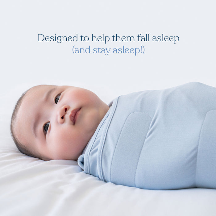 A baby wrapped in a light blue HALO Swaddle SuperSoft Bamboo TOG 2.0 lies on a white bed. Above, text reads: Designed to help them fall asleep (and stay asleep!).