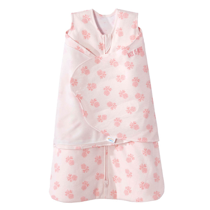 The HALO Swaddle 100% Cotton TOG 1.5 in pink features a floral rose pattern, sleeveless top, and front zipper. Its adjustable wings ensure a snug fit, promoting healthy hip development and comfort for your baby.