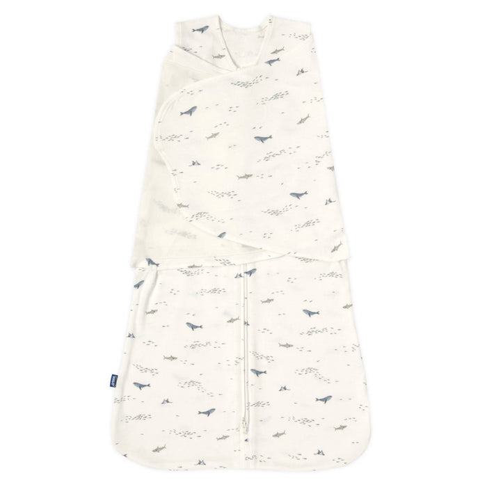 The HALO Swaddle 100% Cotton TOG 1.5 features a wrap-over design with adjustable wings and is adorned with a shark and fish pattern in soothing blue and gray. It boasts soft, cozy fabric and a convenient double zipper down the center.