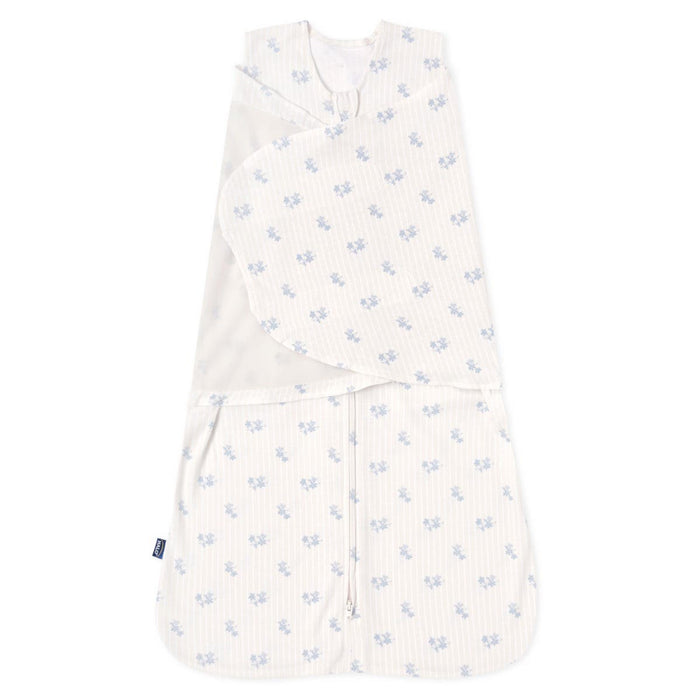 The HALO Swaddle 100% Cotton TOG 1.5 in white features light blue floral patterns on soft fabric, with adjustable wings for a snug fit and promotes healthy hip development. The widened bottom ensures comfort, and theres a small tag on the left edge.