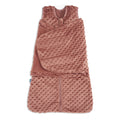 The HALO Swaddle Plushy Dot Velboa TOG 3.0 is a soft, pinkish-brown sleeveless sleep sack with textured raised dots, a front zipper, and an attached adjustable swaddle wrap for a cozy 3-in-1 sleep solution.