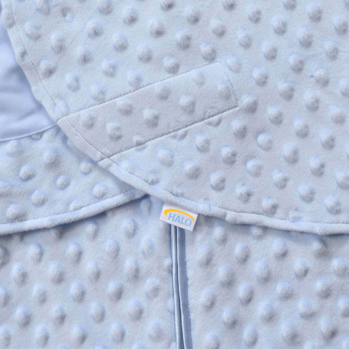 Close-up of the Swaddle Plushy Dot Velboa TOG 3.0, a light blue textured baby blanket by HALO, featuring raised polka dots and a small HALO tag. Its soft, plush fabric ensures comfort and promotes healthy hip development, inspired by the SleepSack Swaddle.