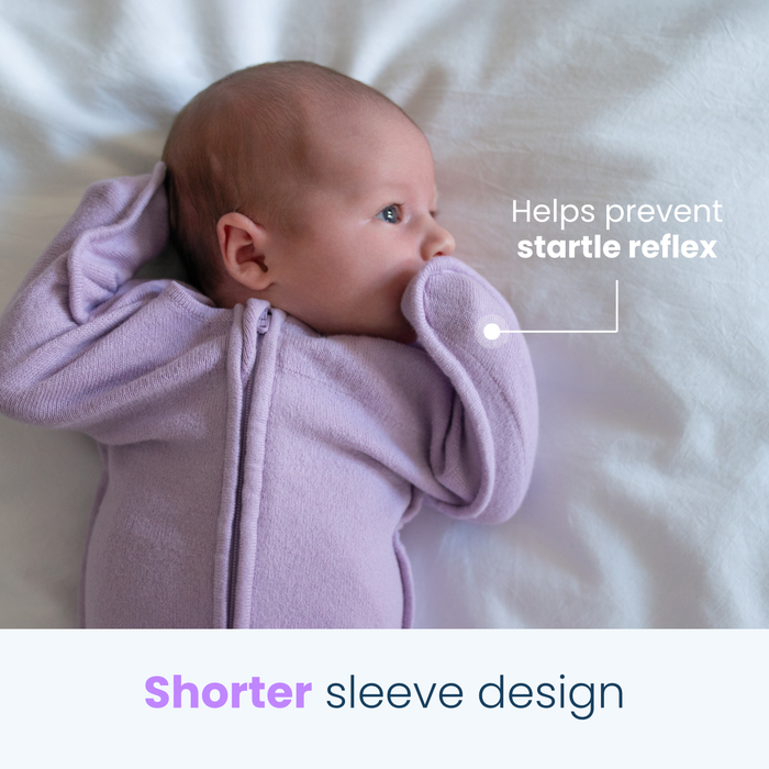 New sentence: A baby in a lavender HALO SwaddleStretch™ Newborn Swaddle TOG 0.5 lies on a white blanket, sucking on its sleeve. Text reads, Helps prevent the startle reflex and features a shorter sleeve design—just what you need from HALO.