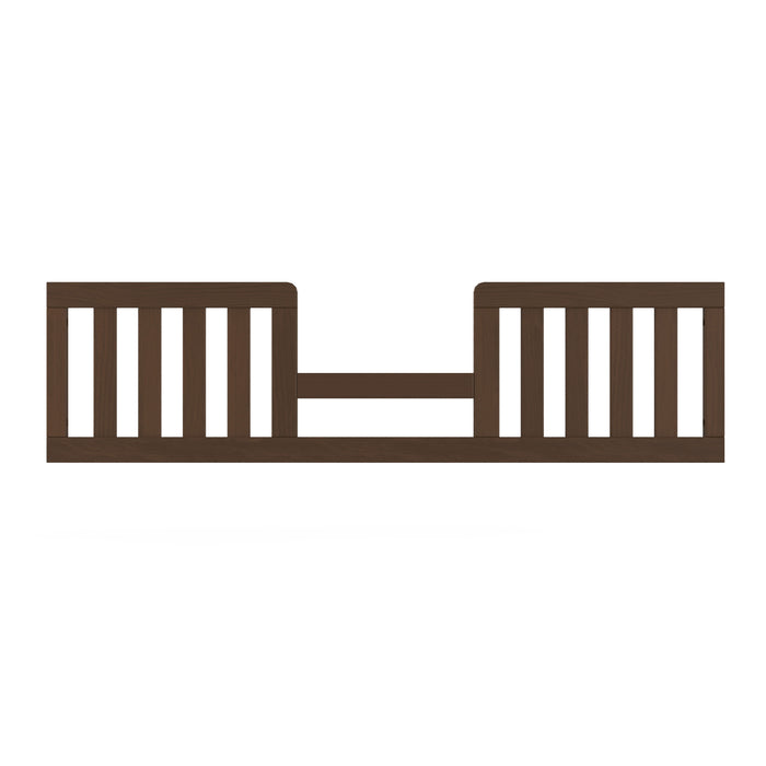 The Child Craft Toddler Guard Rail in Toasted Chestnut features vertical slats and an open center for safety. Designed for crib conversion, it attaches to your bed and has baby-safe finishes. Shown against a plain white background.
