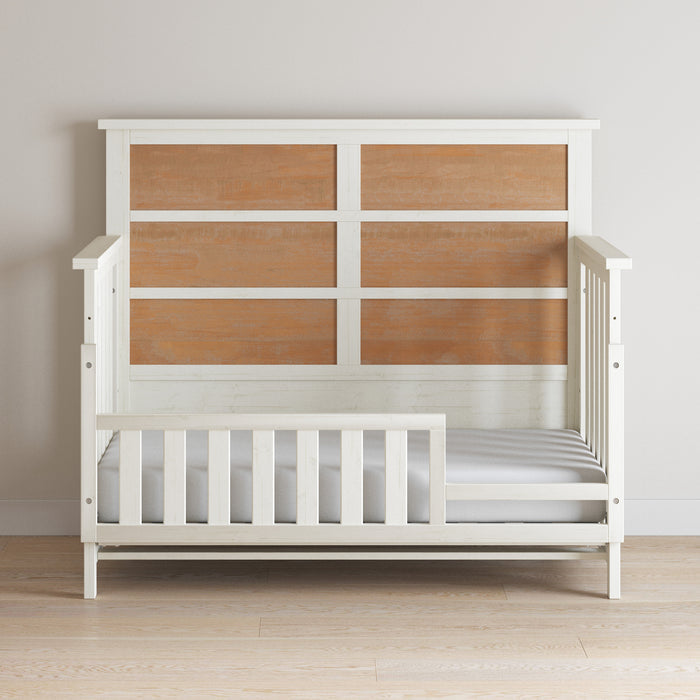 The Child Craft Toddler Guard Rail in White/Brown features a high headboard with light brown panels, low side rails, and gray mattress, set on a light wood floor against a plain wall—perfect for crib conversion.