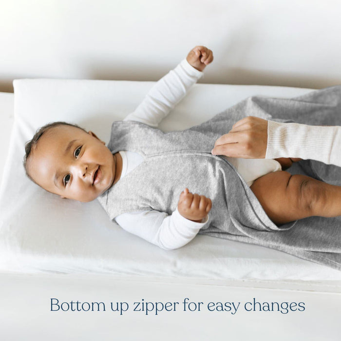 A baby lies on a changing table wearing a gray HALO Eric Carle The Very Hungry Caterpillar 100% Cotton Wearable Blanket TOG 0.5, while an adult zips it up from the bottom. Text below reads: Bottom up zipper for easy changes.